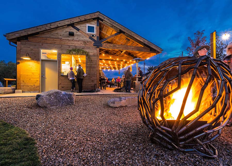 A closeup of the custom-designed iron ball firepit in the foreground with the wooden bar and open-air seating pavilion 